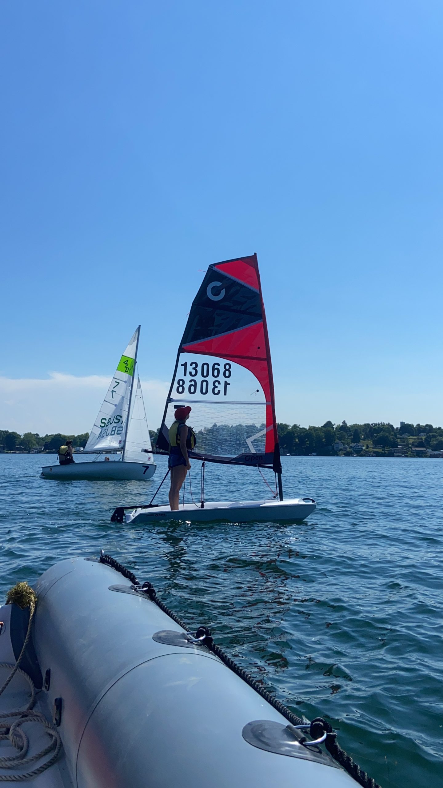 two small sailboats on the water, a O'pen Skiff or O'pen BIC and a 420 sail boat they are sailing on a lake or a body of water it is a windy day